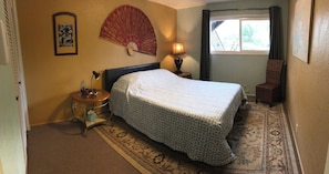 Quarto de hotel com cama, mesa de cabeceira, luminária, cadeira e janela com cortinas.