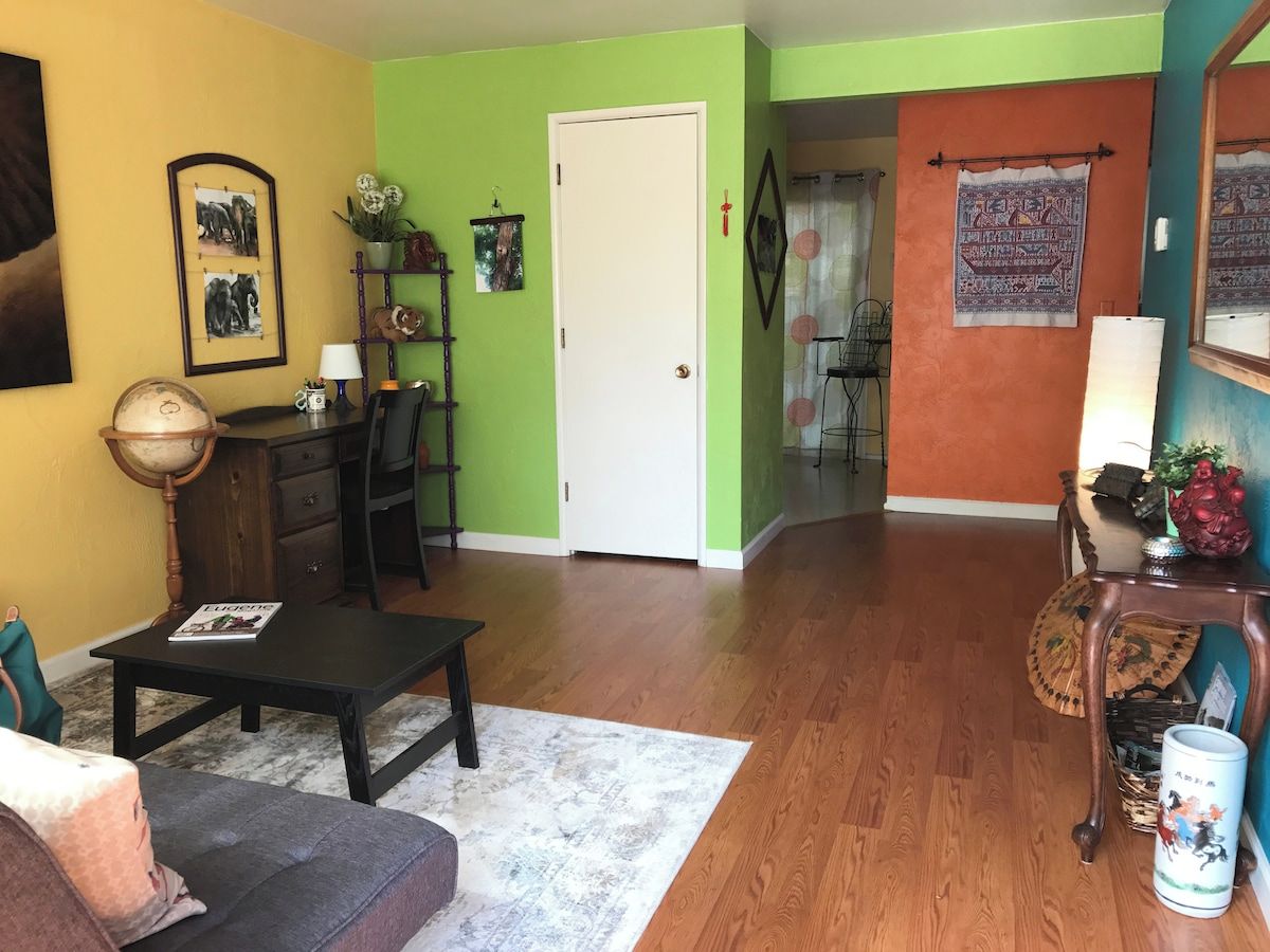A living room with a sofa, a coffee table, and a wooden floor. There is a door leading to another room.