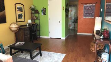 A living room with a sofa, a coffee table, and a wooden floor. There is a door leading to another room.