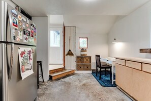 Eine Küche mit Kühlschrank, Holzschränken, einem Esstisch und einem Besen.