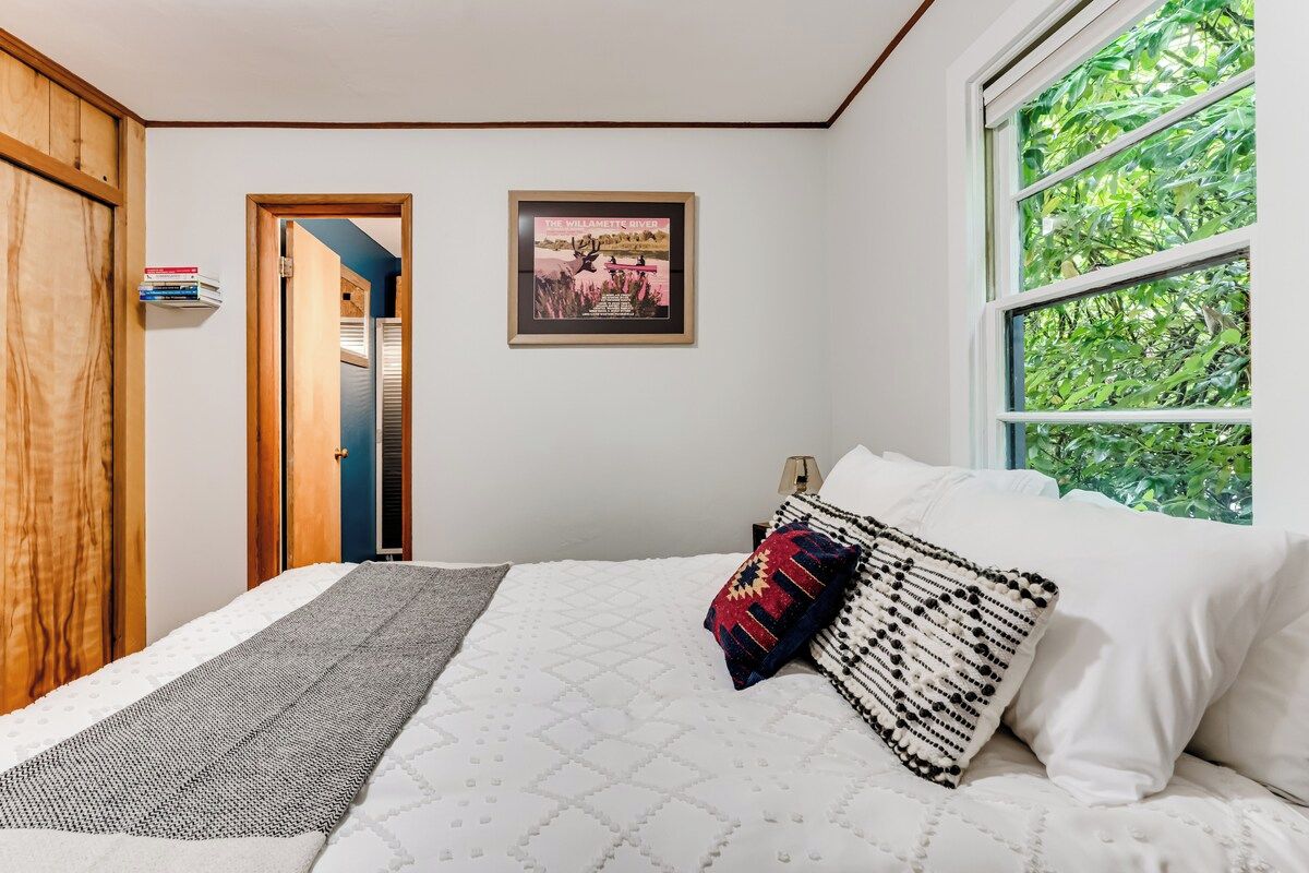 Ein Schlafzimmer mit einem Bett, Kissen, einem gerahmten Bild, einem Fenster und einer Tür.