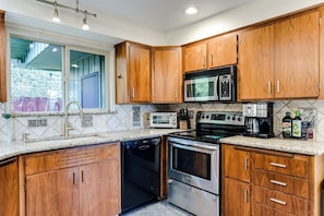 A kitchen with wooden cabinets, a microwave, a toaster, and a dishwasher. - Mid-Century Modern Retreat Near UO & Hayward Field (Eugene)