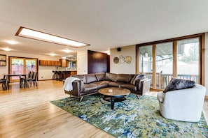 A spacious living area with a leather sectional sofa, a round coffee table, and a white armchair. A dining area with chairs and a table is visible in the background. - Mid-Century Modern Retreat Near UO & Hayward Field (Eugene)