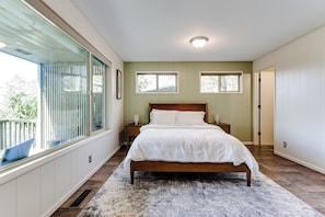 A bedroom with a large bed, two bedside tables, a window, and a door. - Mid-Century Modern Retreat Near UO & Hayward Field (Eugene)