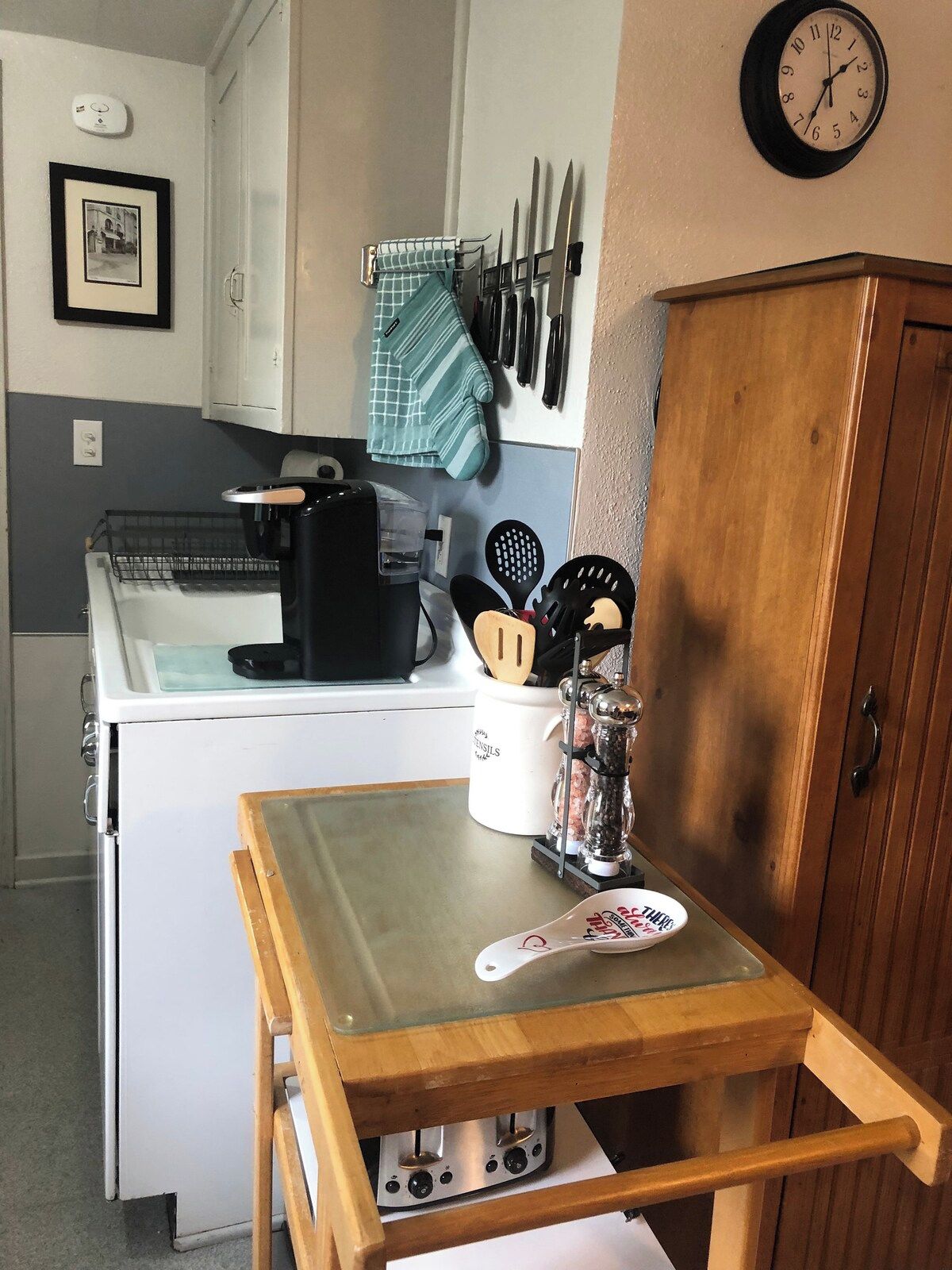 A compact kitchen with a white stove, a coffee maker, and a wooden table with a plate.