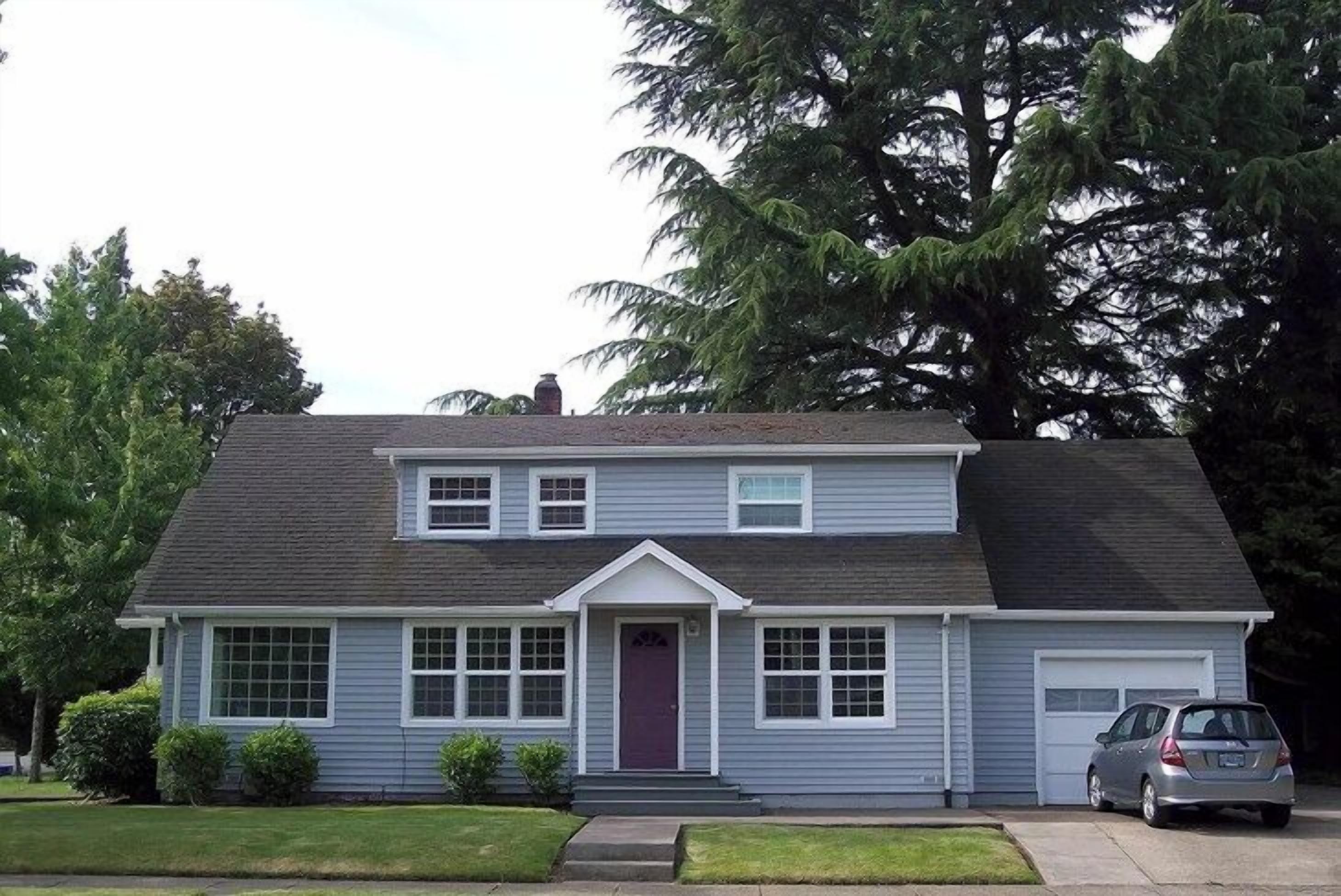 A two-story house with a front garage, a red door, and a car parked in the driveway.