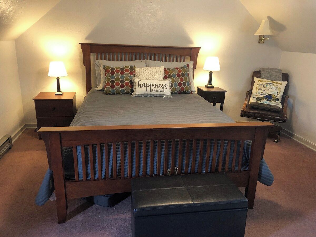 A bedroom with a wooden bed, two bedside tables with lamps, a bench, and a chair.