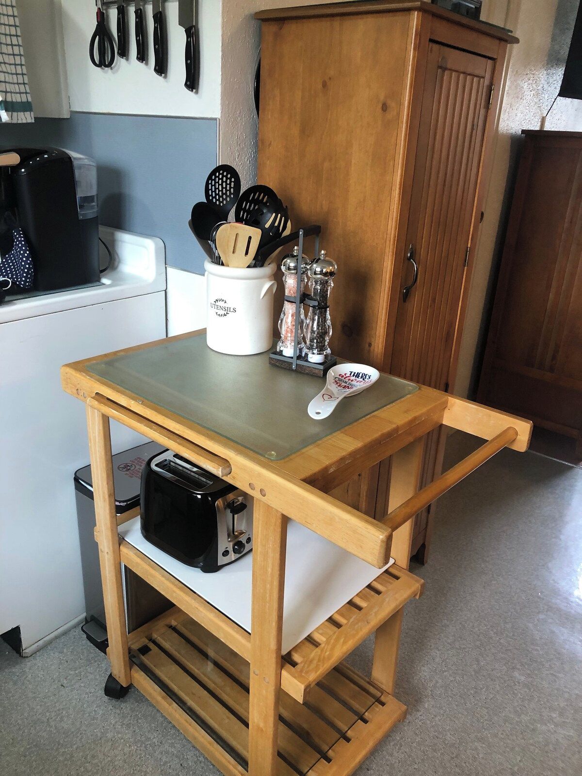 A kitchen area with a wooden cart, a coffee maker, and a cabinet.