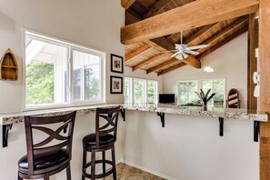 A kitchen with a high ceiling, wooden beams, a ceiling fan, and a window overlooking greenery. - Waterfront House w/ Private Dock & Game Room (Veneta)
