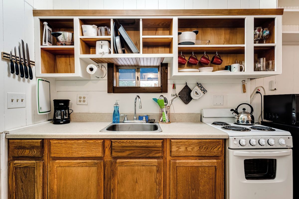 Una cocina con armarios de madera, horno empotrado y ventana sobre el fregadero.