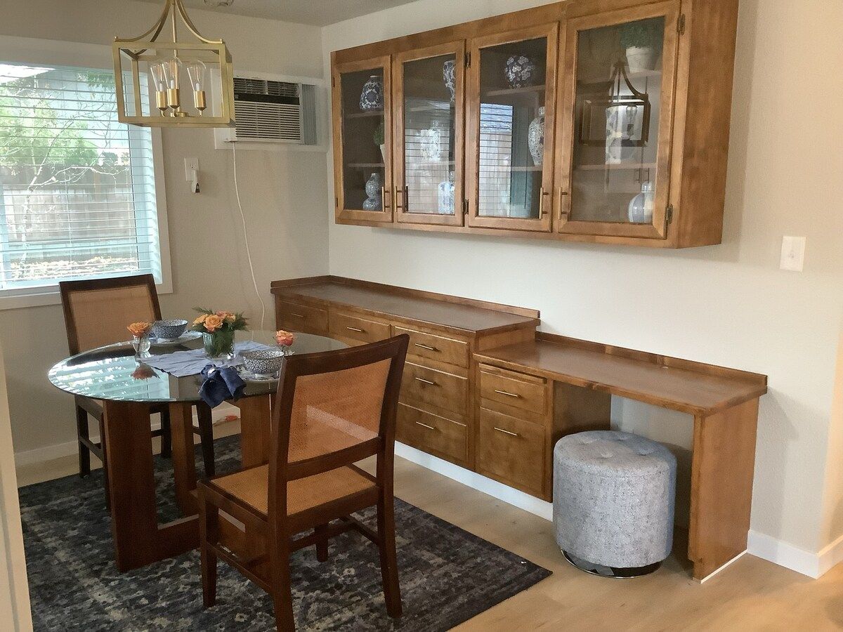 A dining area with a round table, chairs, a cabinet with glass doors, and a small stool.