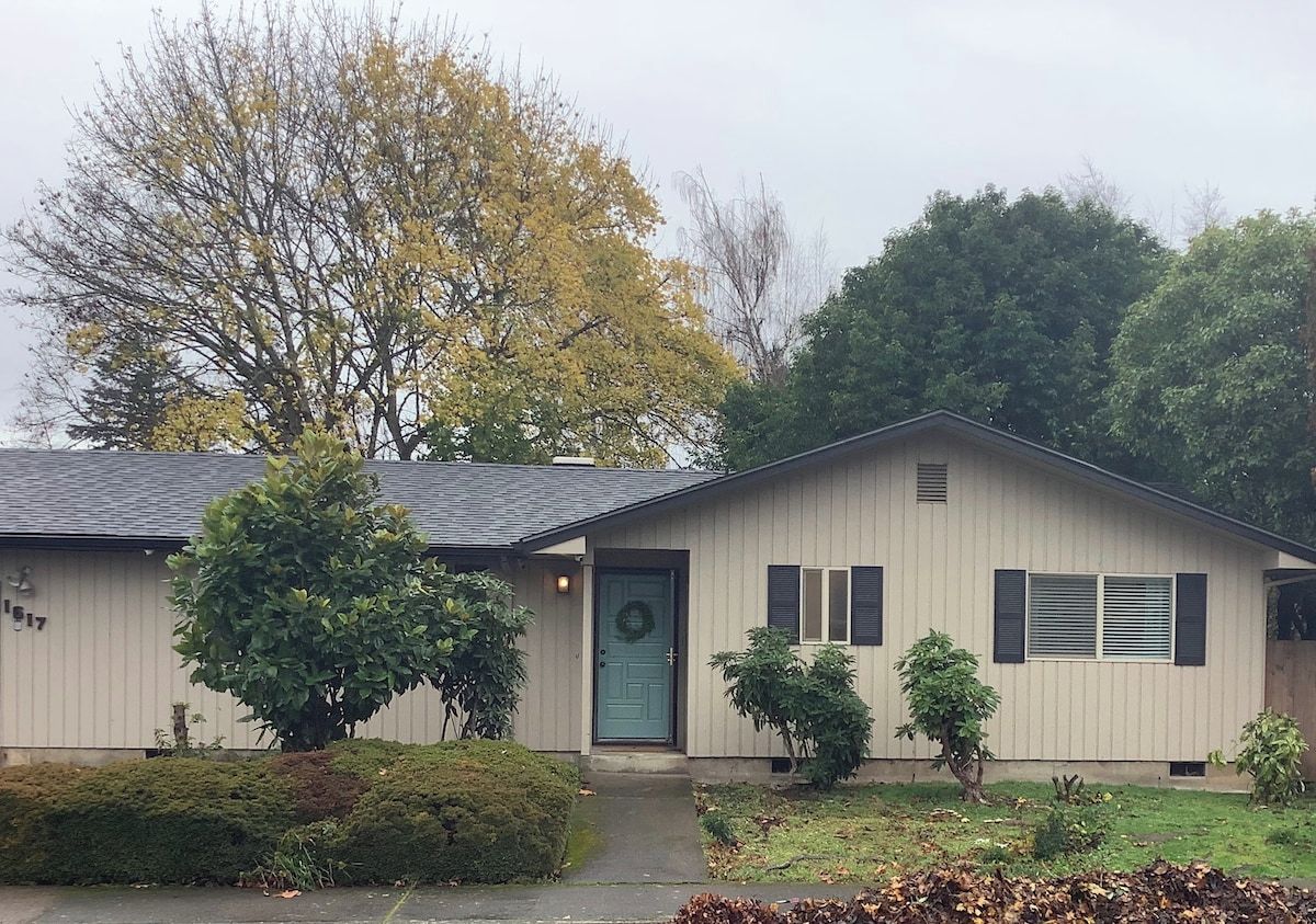 A single-story house with a front door, a small porch, and a front yard with a tree and shrubbery.