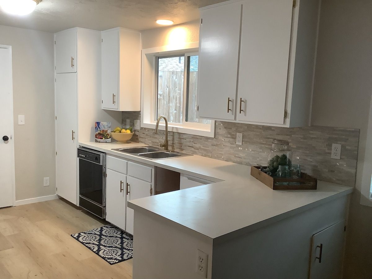 A modern kitchen with white cabinetry, a dishwasher, and a window above the sink.