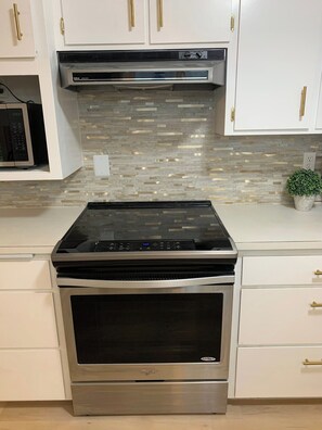 A kitchen with a built-in stove, microwave, and oven, white cabinets with gold handles, and a tiled backsplash. - Remodeled House near Downtown Eugene w/ Free (Eugene)