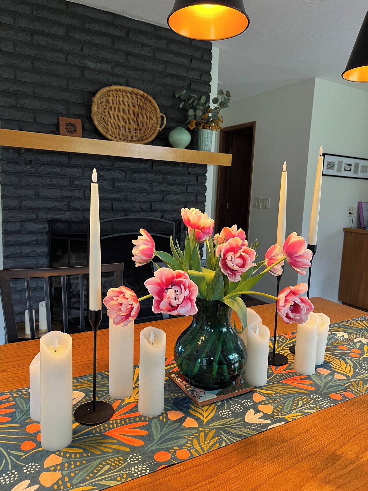 Ein Esstisch mit einer floralen Tischdekoration, Kerzen und einer gemusterten Tischmatte.