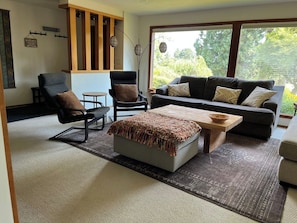 Ein Wohnzimmer mit einer Couch, Sesseln, einem Couchtisch und einem großen Fenster.