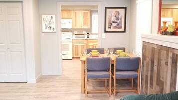 A dining area with a table set for two, a kitchen in the background, and a green sofa in the foreground.