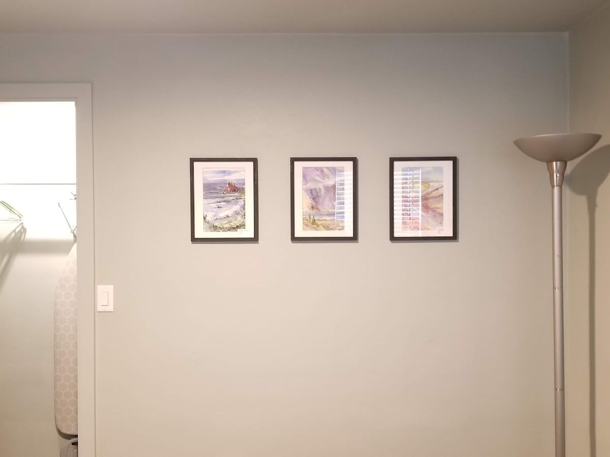 Pareda com três obras de arte emolduradas, uma luminária e uma porta.