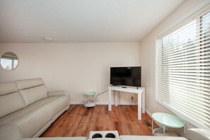 A living room with a sofa, a television on a stand, a small table, and a window with blinds. - West Hills Retreat with Reclining Couch & King Bed (Eugene)