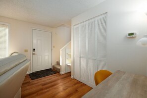 A room with a wooden floor, a white door, a white closet with louvered doors, a small staircase, and a thermostat on the wall. - West Hills Retreat with Reclining Couch & King Bed (Eugene)