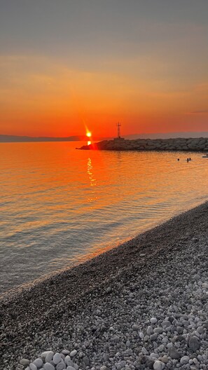 Un coucher de soleil sur une plage de galets, avec une eau calme qui reflète le ciel.