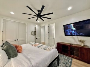 A bedroom with a bed, a TV, a ceiling fan, and a wooden cabinet. - Hollow Sands Guest Suite | Hot Tub | Pool (Hurricane)