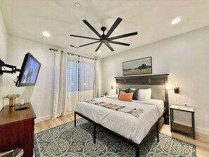 A modern bedroom with a bed, a desk, a television, and a ceiling fan. - Hollow Sands Guest Suite | Hot Tub | Pool (Hurricane)