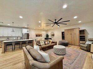 A modern living room with a sofa, ottoman, and a dining area with a table and chairs. - Hollow Sands Guest Suite | Hot Tub | Pool (Hurricane)