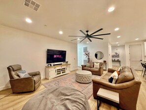 A modern living room with a flat-screen TV, leather sofas, a ceiling fan, and a wooden entertainment unit. - Hollow Sands Guest Suite | Hot Tub | Pool (Hurricane)