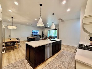 A modern kitchen with a central island, dark cabinetry, and pendant lighting. - Hollow Sands Retreat | Hot Tub | Pool | Duplex (Hurricane)