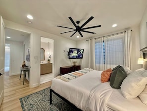 A bedroom with a bed, a television, a ceiling fan, and a window with curtains. - Hollow Sands Retreat | Hot Tub | Pool | Duplex (Hurricane)