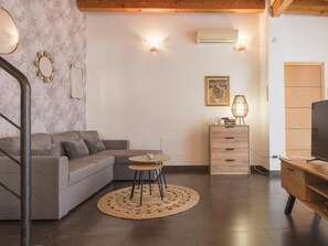 A modern living room with a grey sofa, a small round table, a wooden cabinet, and a TV stand. - Ladera Machin Apartment (Toledo)