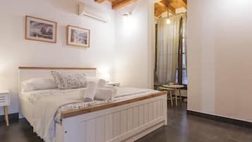 A bedroom with a bed, bedside tables, an air conditioning unit, and a window with curtains.
