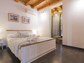 A bedroom with a bed, bedside tables, an air conditioning unit, and a window with curtains. - Ladera Machin Apartment (Toledo)