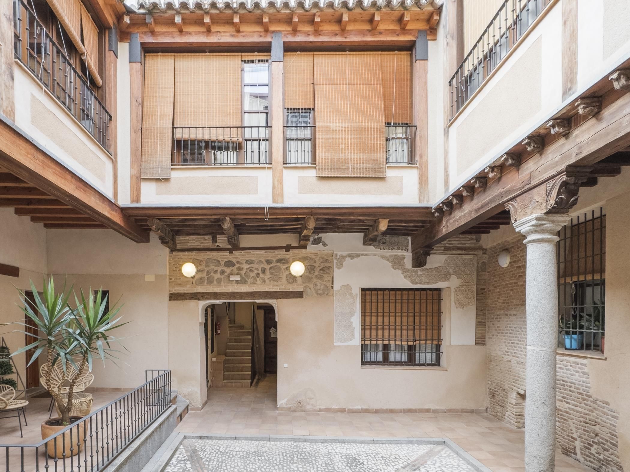 Un patio con suelo de piedra, un balcón de madera y una escalera que lleva a un nivel superior.
