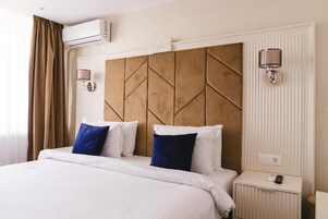 A hotel room with a large bed, two bedside lamps, a nightstand, and an air conditioning unit.