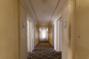 A hotel corridor with a patterned carpet, white walls, and doors on both sides.