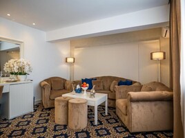 A modern living room with a beige sofa set, a white coffee table, and two side tables. There is a decorative bowl on the coffee table and a mirror on the wall.
