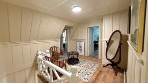 Una escalera con barandal blanco que lleva a una plataforma donde hay una silla de mimbre, una mesita redonda y un espejo.