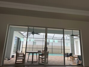 Eine Glasschiebetür führt zu einem Garten mit Pool, Terrassenmöbeln und Deckenventilatoren.