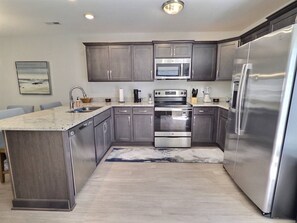 A modern kitchen with stainless steel appliances, grey cabinetry, and a light wood floor. - Nautilus Landing Getaway (Clarksville)