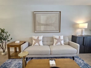 A living room with a sofa, two starfish pillows, a side table, a lamp, and a coffee table. - Nautilus Landing Getaway (Clarksville)