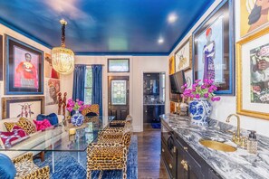 Ein modernes Wohnzimmer mit einem Glastisch, Leopardenprint-Stühlen, einer Chandelüster und einer Küche mit Marmorarbeitsplatten.