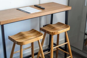 A wooden table with a remote control and a menu on it, and two wooden stools with metal legs. - Sutherland Apartments - Apt 25 (London)