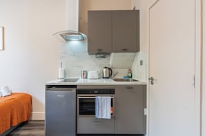 A compact kitchenette with a built-in dishwasher, a microwave, and a small oven. - Sutherland Apartments - Apt 25 (London)