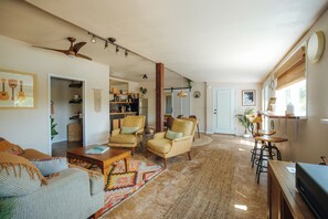 A spacious living room with a large window, a ceiling fan, and a dining area with a table and chairs.