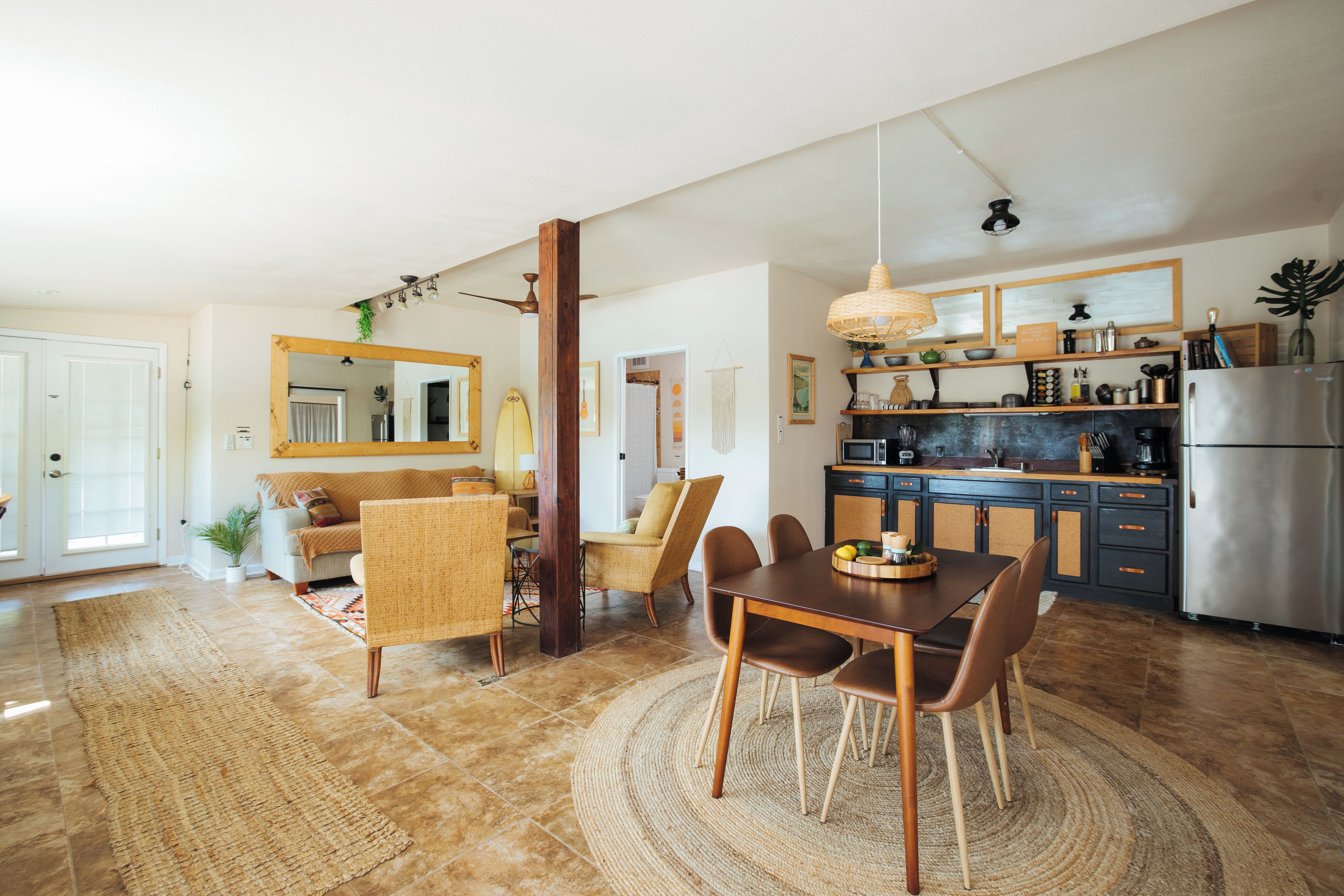 A modern kitchen with a dining area, featuring a central island, wooden chairs, and a large mirror.