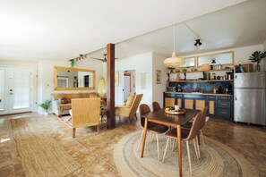 A modern kitchen with a dining area, featuring a central island, wooden chairs, and a large mirror.
