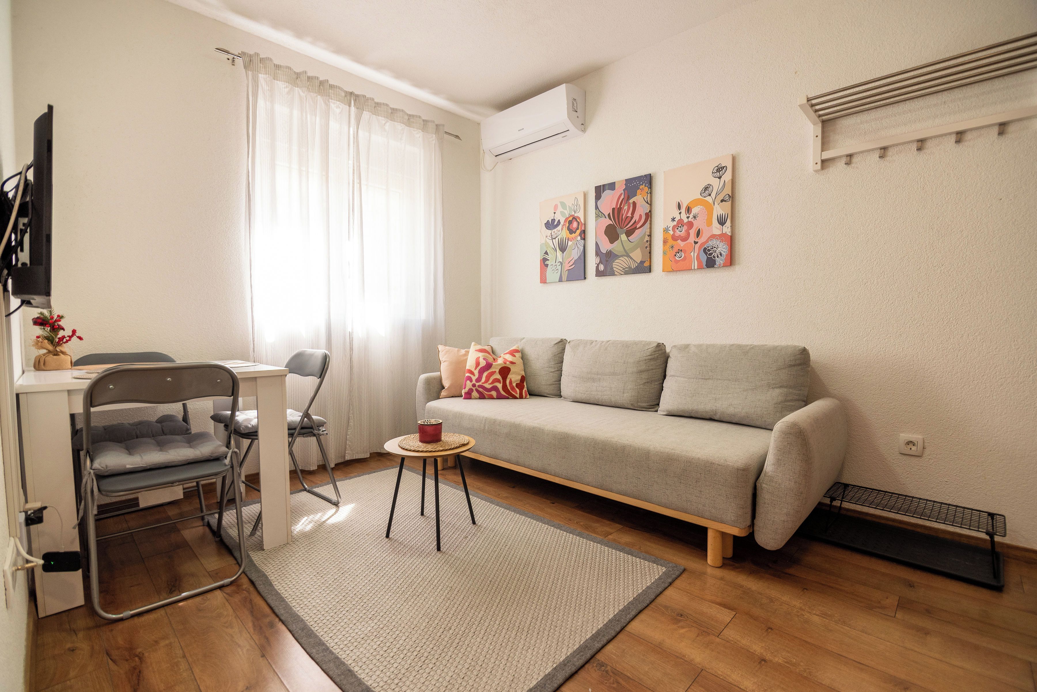 A modern living room with a sofa, a dining table with chairs, a flat-screen TV, and artwork on the wall.
