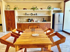 A dining area with a wooden table and chairs, a kitchen in the background with shelves and appliances, and a refrigerator. - Perfect beachfront 3-bedroom house with AC in tranquil Chelem (Chelem)